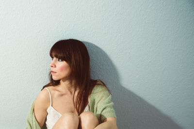 Young woman sitting against wall