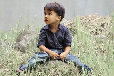 Boy looking away while sitting on grassy field