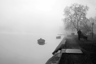 Rear view of man walking on lakeshore against sky during foggy weather