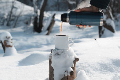 Male hand pouring hot tea into a mug from a thermos in the winter forest. warming drink 