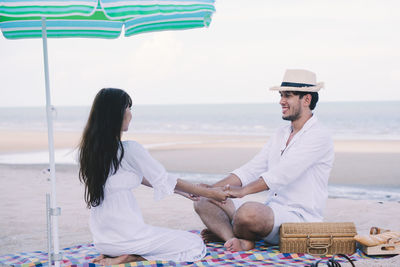 Young couple holding hands while sitting at beach