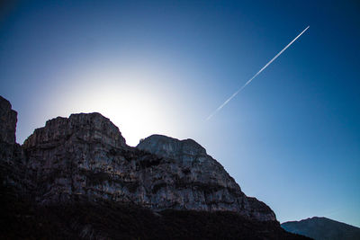 Low angle view of vapor trail over rock formations against clear blue sky