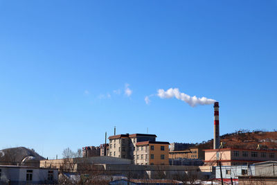 Smoke emitting from factory against blue sky