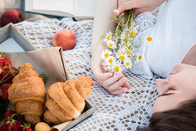 High angle view of woman holing flowers lying on bed with food