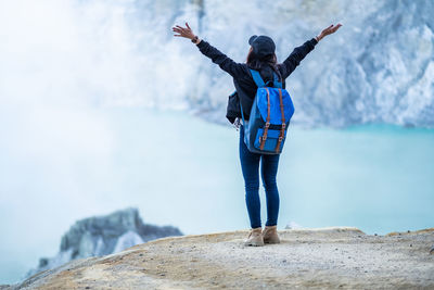 Full length of woman with arms raised standing on rock by sea