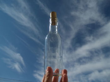 Person holding bottle against sky