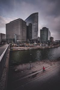 Modern buildings by river against sky in city