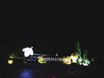 Illuminated text on tree in city against sky at night