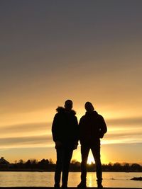 Silhouette friends standing by lake during sunset