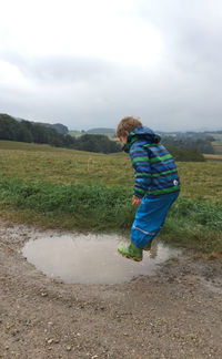 View of boy jumping in puddle against sky