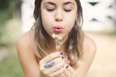 Portrait of young woman blowing dandelion seeds