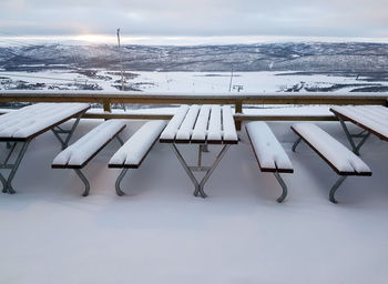 Deck chairs on snow covered mountain against sky