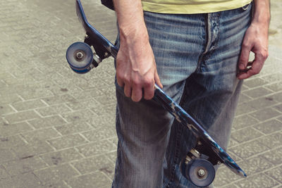 Midsection of man holding skateboard while standing on street