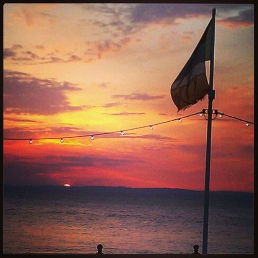 sunset, sea, horizon over water, sky, water, orange color, transfer print, scenics, beauty in nature, tranquility, silhouette, tranquil scene, auto post production filter, cloud - sky, nature, cloud, idyllic, outdoors, flag, beach