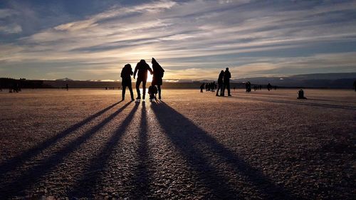 Silhouette people on ice rink against sky during sunset
