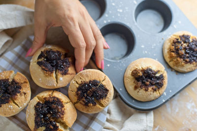 Cropped hand of woman picking muffins from tin on table 