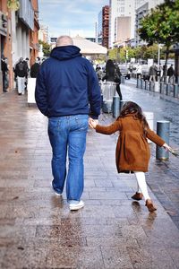 Rear view of father and daughter walking on street in city