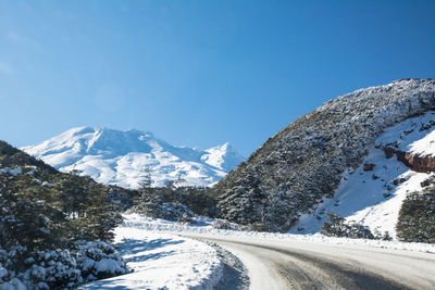 Road amidst snowcapped mountains against clear blue sky