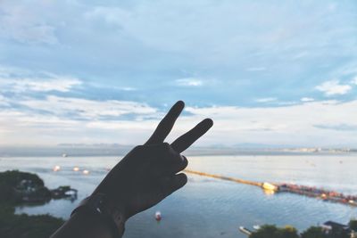 Person hand by sea against sky