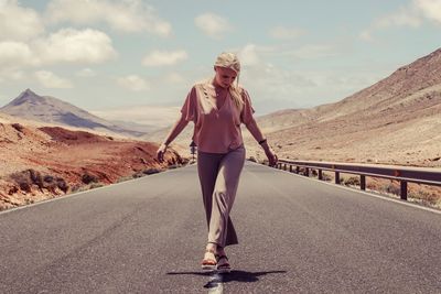 Full length portrait of woman standing on road against sky