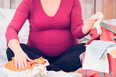 Low section of woman packing clothes in bag while sitting on bed