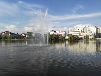 Fountain in lake against buildings in city