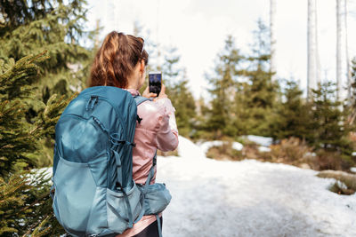 Girl tourist with a backpack on her back takes a photo on a mobile phone while walking in the forest