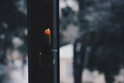 Lit candle on closed window at home during winter