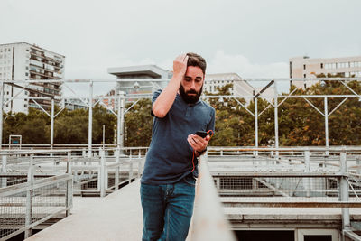 Young man using mobile phone while standing on railing