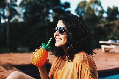 Smiling young woman in sunglasses having drink at poolside