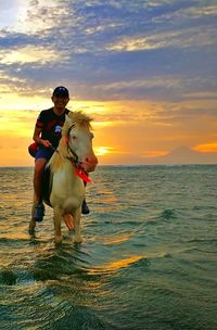 Woman with dog on sea against sky during sunset
