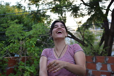Woman laughing against trees