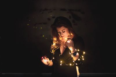 Young woman holding illuminated string light at dark room