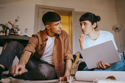 Male freelancer discussing with female colleague holding laptop while sitting at home office
