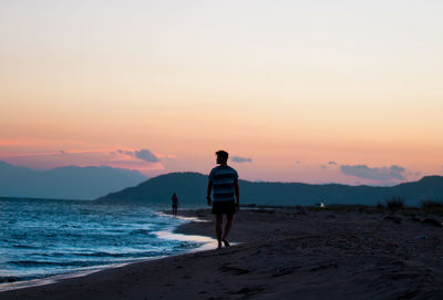 Rear view of man walking on shore at beach during sunset