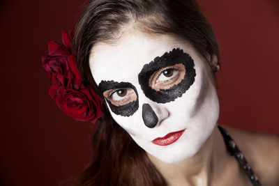 Woman with makeup of la santa muerte with red roses in front of a red background
