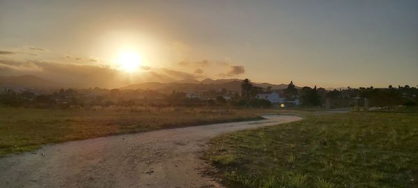 Road amidst field against sky during sunset