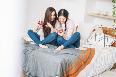 Woman showing mobile phone to friend having wine at home