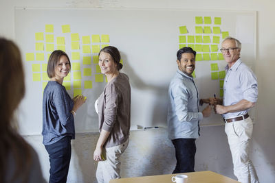 Happy business people standing by whiteboard at office