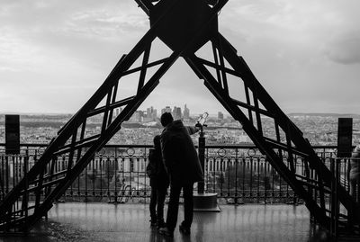 Man and child standing in eiffel tower against sky in city