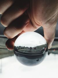 Cropped hand holding crystal ball against road