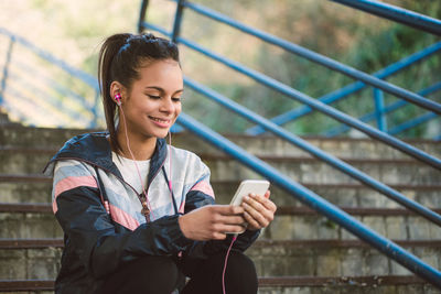 Young woman using phone while standing on railing