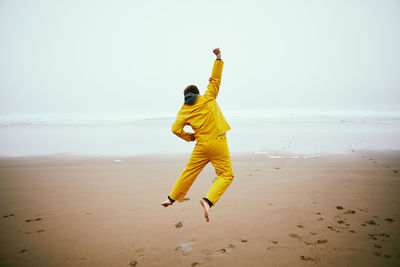 Rear view of man jumping at beach against clear sky