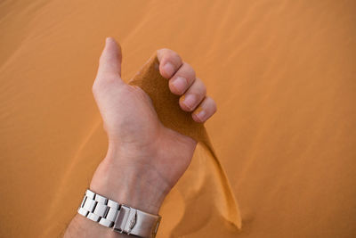 Cropped hand of man playing with sand at desert