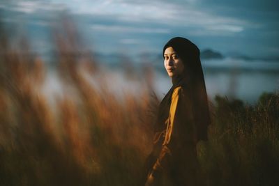 Side view portrait of young woman standing amidst plants on field