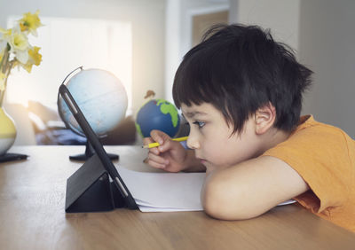 Boy looking at mini computer while doing home work at home