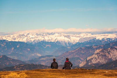 Rear view of men sitting on mountain against sky