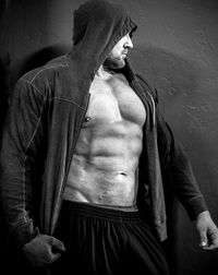 Muscular man wearing hooded shirt while standing against wall