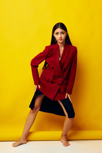 Portrait of young woman standing against yellow background