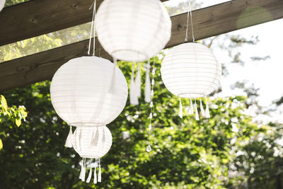 Low angle view of white lanterns hanging from pergola at patio